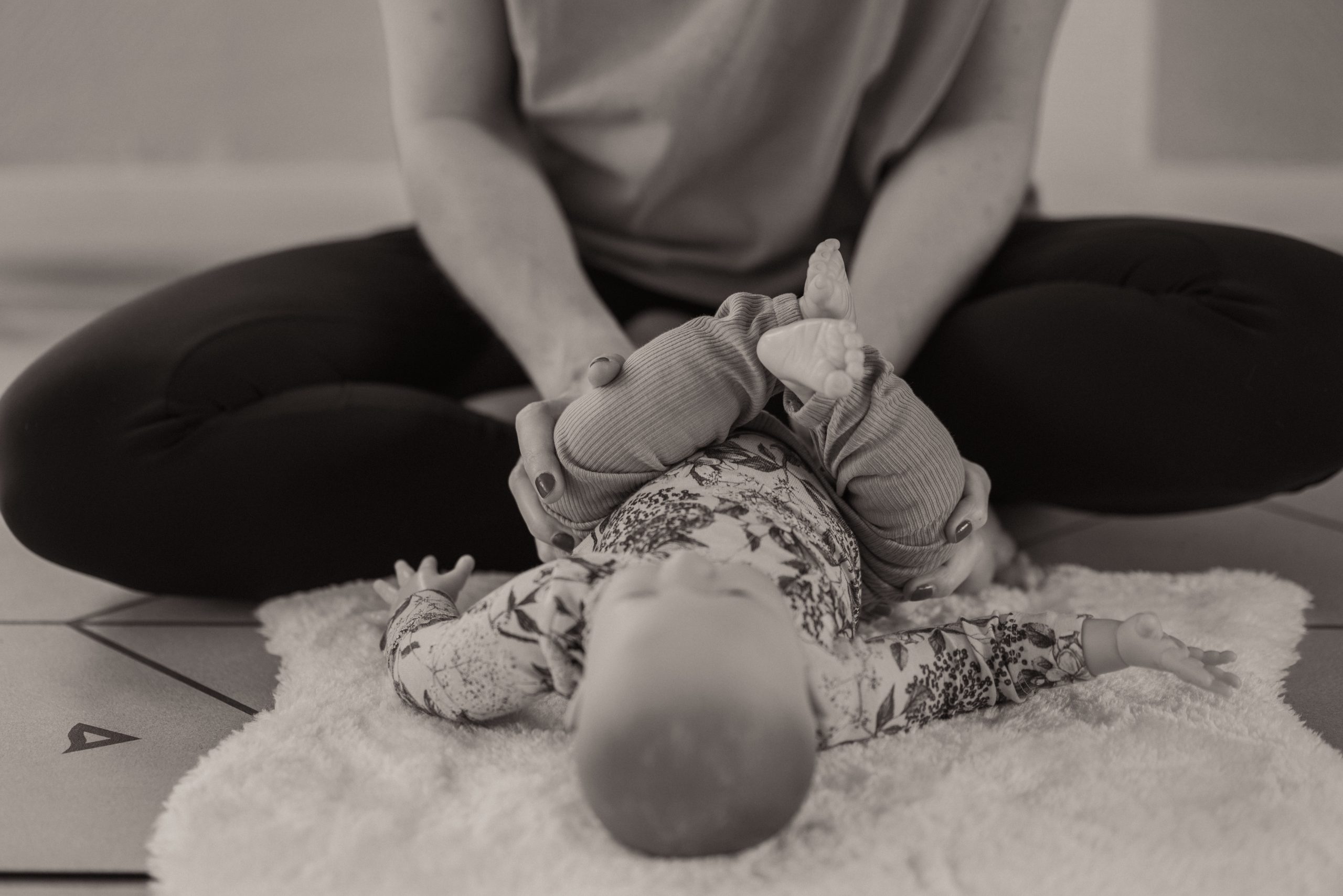 Babymassage im Kurs: Kursleiterin massiert sanft die Beine eines entspannten Babys auf einer weichen Decke.